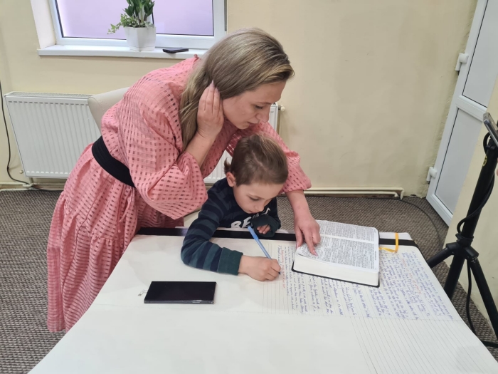 母親指導男童如何抄寫聖經。（圖／翻攝自FB@Muzeul Bibliei）